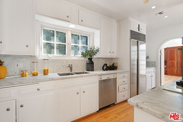 kitchen with sink, stainless steel appliances, tasteful backsplash, white cabinets, and light wood-type flooring