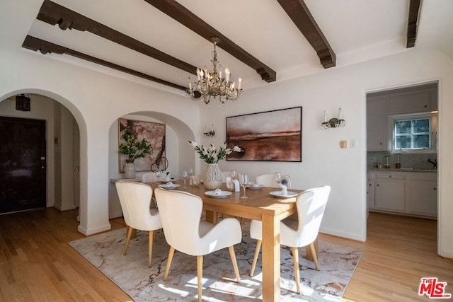 dining room with sink, beamed ceiling, a notable chandelier, and light wood-type flooring