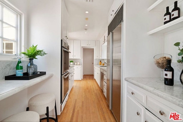 kitchen with backsplash, white cabinetry, light stone countertops, and light wood-type flooring