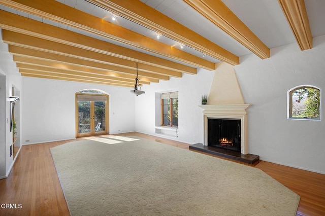 unfurnished living room with hardwood / wood-style floors, beamed ceiling, french doors, a fireplace, and rail lighting