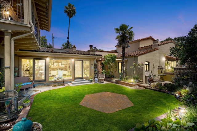 back house at dusk featuring a patio area and a lawn