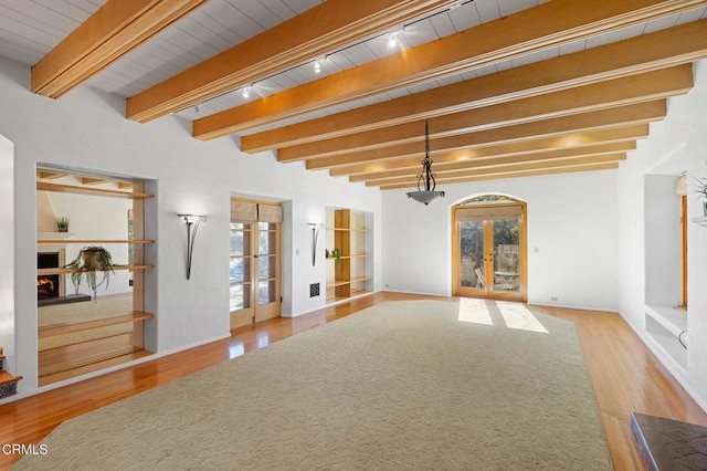 unfurnished living room featuring light wood-type flooring, rail lighting, french doors, and beamed ceiling