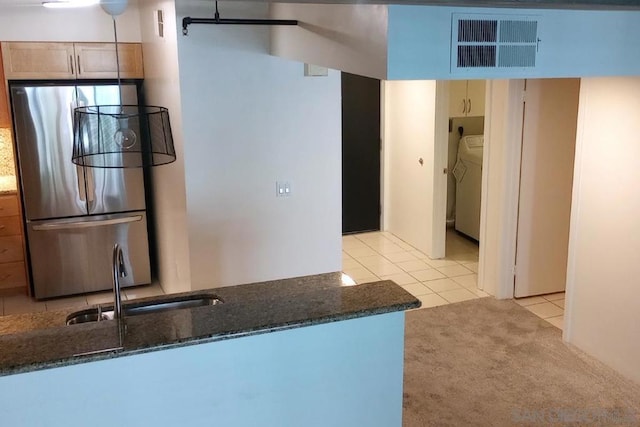 kitchen featuring stainless steel refrigerator, sink, kitchen peninsula, dark stone counters, and light tile patterned floors