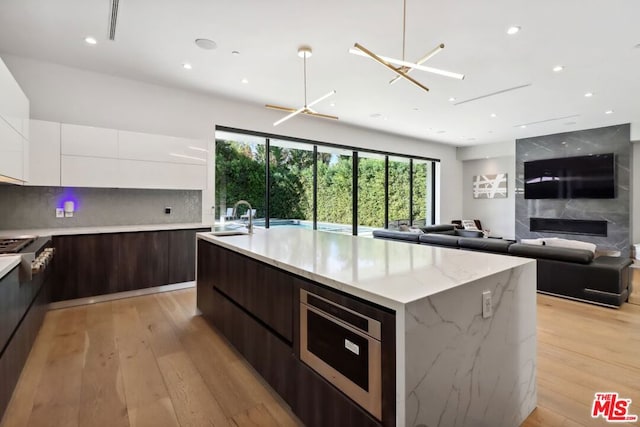 kitchen featuring white cabinets, dark brown cabinetry, light hardwood / wood-style flooring, and an island with sink