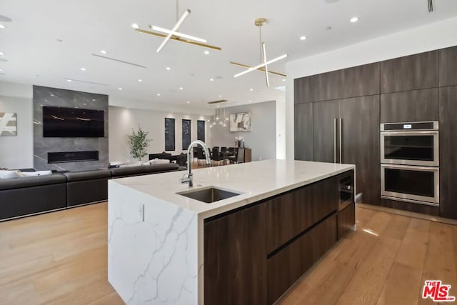 kitchen with a large island with sink, an inviting chandelier, hanging light fixtures, sink, and light hardwood / wood-style flooring