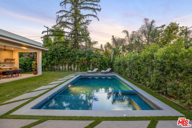 pool at dusk with an in ground hot tub, a yard, and a patio