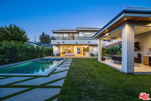 back house at dusk with a lawn, a patio area, a balcony, and an outdoor hangout area