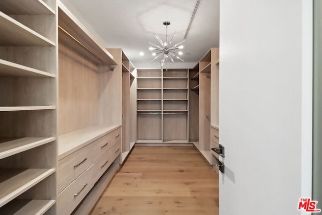 spacious closet with light hardwood / wood-style floors and a notable chandelier