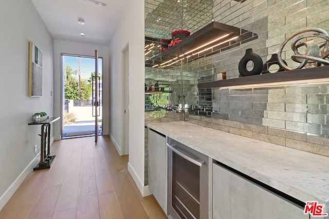 bar with backsplash, light hardwood / wood-style flooring, wine cooler, and light stone counters