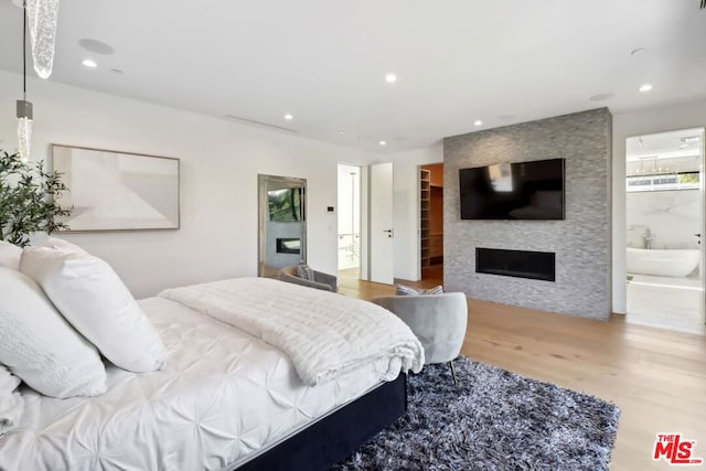 bedroom featuring a walk in closet, a large fireplace, hardwood / wood-style flooring, and ensuite bath