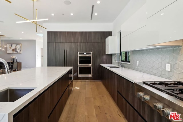 kitchen with white cabinetry, sink, hanging light fixtures, stainless steel appliances, and light wood-type flooring