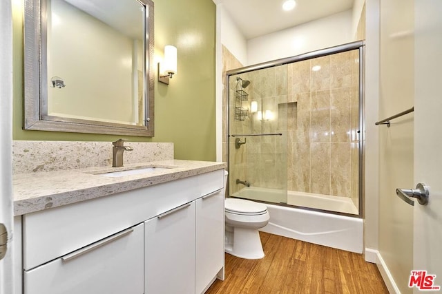 full bathroom with hardwood / wood-style floors, vanity, enclosed tub / shower combo, and toilet