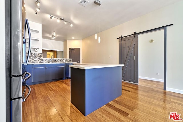 kitchen featuring blue cabinets, a kitchen island, a barn door, stainless steel refrigerator, and hanging light fixtures