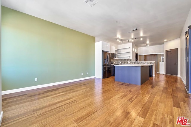 kitchen with stainless steel fridge, light wood-type flooring, a kitchen island, a barn door, and white cabinetry