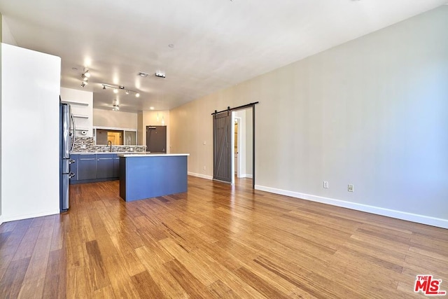 kitchen featuring backsplash, stainless steel fridge, a barn door, a kitchen island, and wood-type flooring