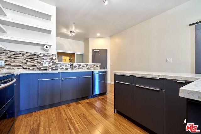 kitchen featuring tasteful backsplash, a barn door, light hardwood / wood-style flooring, stainless steel dishwasher, and blue cabinets