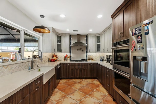 kitchen with tasteful backsplash, stainless steel appliances, hanging light fixtures, and wall chimney range hood