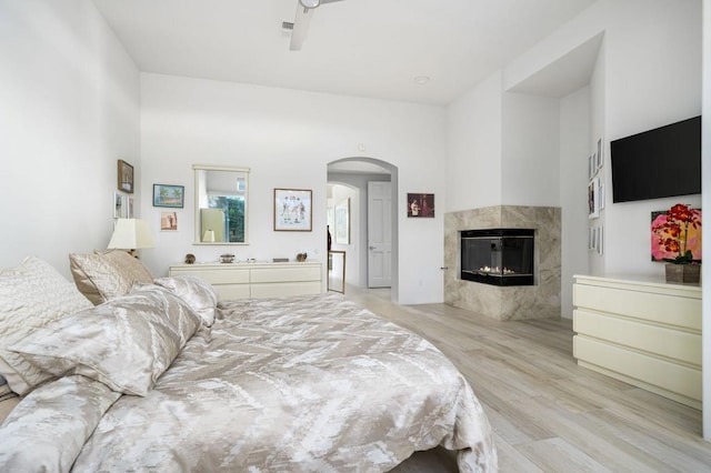 bedroom featuring ceiling fan, light hardwood / wood-style flooring, a high ceiling, and a tiled fireplace