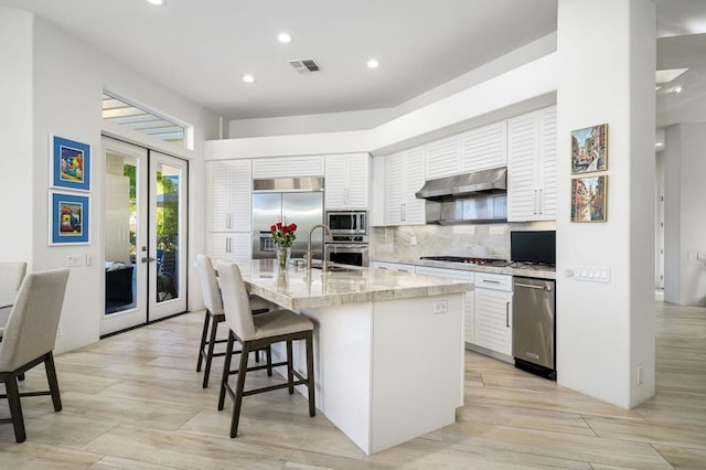 kitchen featuring white cabinetry, french doors, built in appliances, extractor fan, and a kitchen island with sink