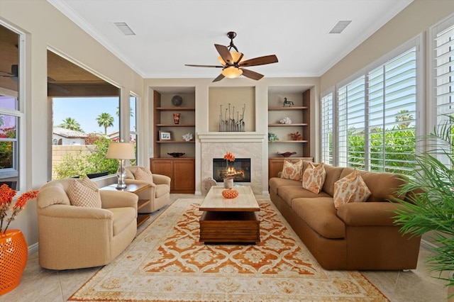 living room with a fireplace, built in shelves, ceiling fan, and crown molding