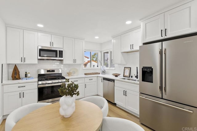 kitchen featuring sink, white cabinetry, stainless steel appliances, light hardwood / wood-style floors, and decorative backsplash