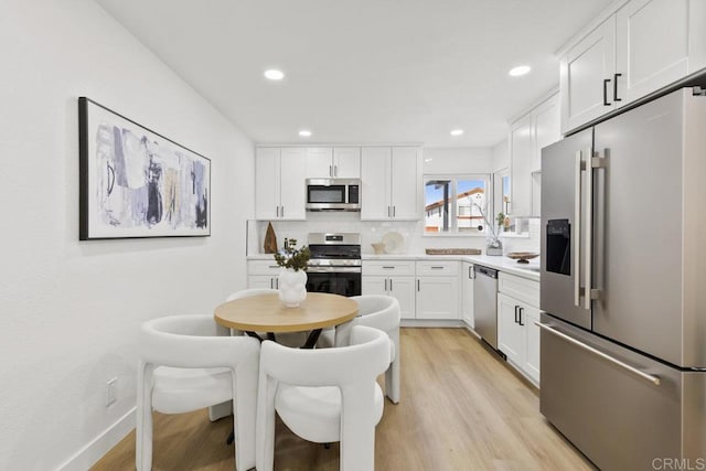 kitchen featuring tasteful backsplash, stainless steel appliances, light hardwood / wood-style floors, and white cabinets