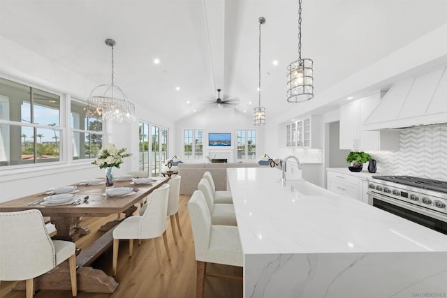 kitchen with backsplash, vaulted ceiling, decorative light fixtures, stainless steel range, and white cabinets