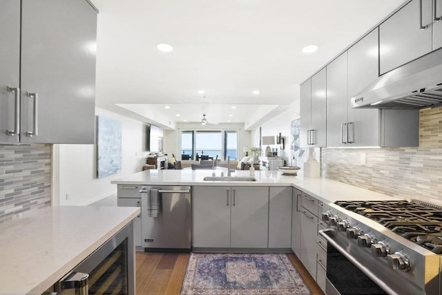 kitchen with dishwasher, range hood, kitchen peninsula, sink, and gray cabinetry