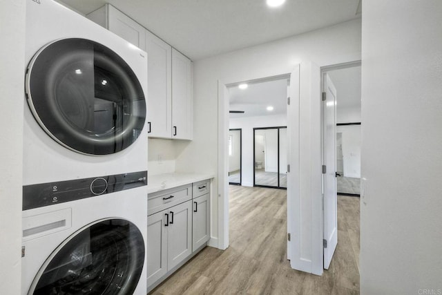 laundry area featuring stacked washer / drying machine, cabinets, and light wood-type flooring