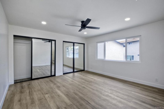 unfurnished bedroom featuring ceiling fan, light hardwood / wood-style flooring, and two closets