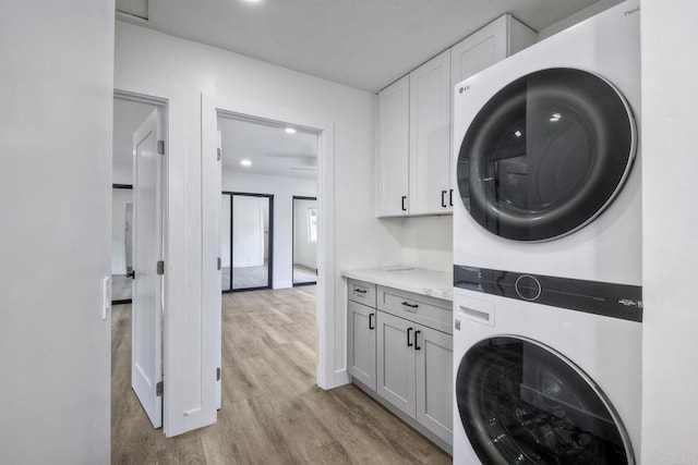 clothes washing area with light hardwood / wood-style floors, cabinets, and stacked washing maching and dryer