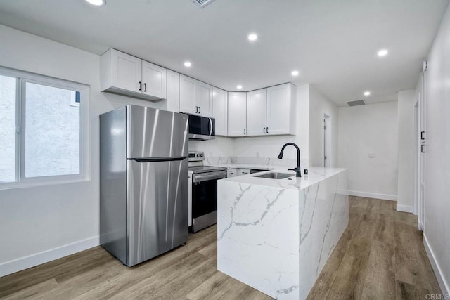 kitchen with light stone countertops, sink, white cabinetry, light hardwood / wood-style floors, and stainless steel appliances