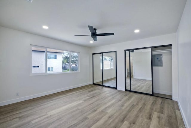 unfurnished bedroom with multiple closets, electric panel, light hardwood / wood-style floors, and ceiling fan