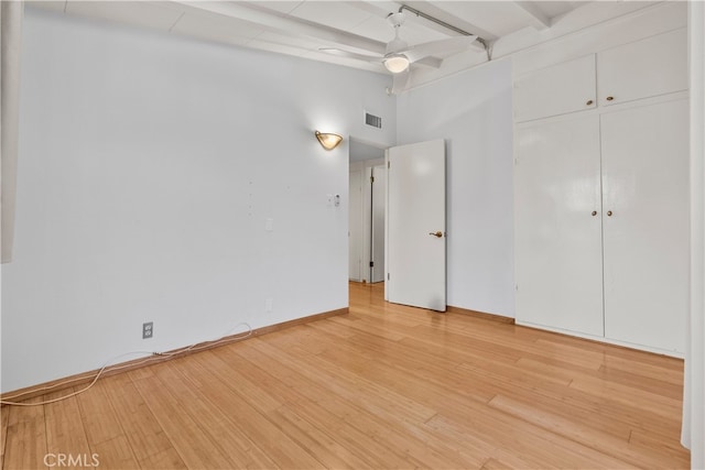 unfurnished bedroom with hardwood / wood-style floors, beam ceiling, ceiling fan, a towering ceiling, and a closet