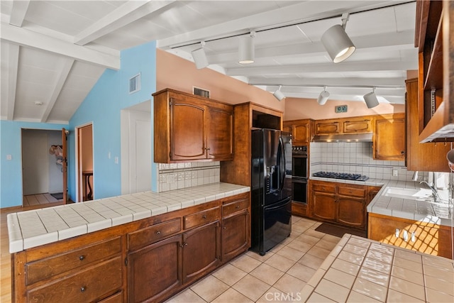 kitchen with tasteful backsplash, rail lighting, tile countertops, black appliances, and lofted ceiling with beams