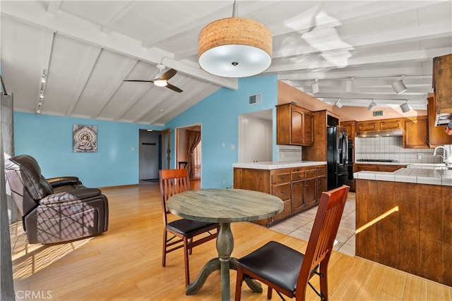 dining space featuring ceiling fan, beamed ceiling, sink, and light wood-type flooring