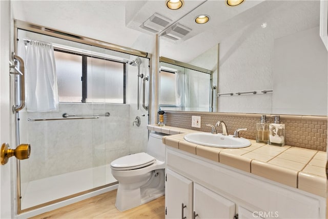 bathroom with hardwood / wood-style floors, backsplash, toilet, a shower with shower door, and vanity