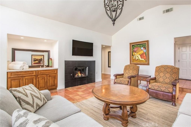 tiled living room featuring a tiled fireplace, high vaulted ceiling, and an inviting chandelier