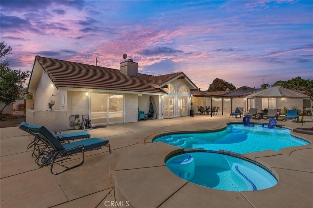 pool at dusk with an in ground hot tub and a patio