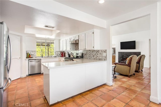 kitchen featuring kitchen peninsula, decorative backsplash, a fireplace, appliances with stainless steel finishes, and white cabinetry