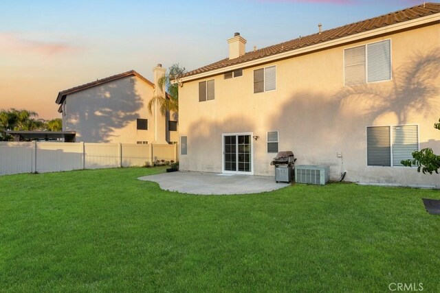 back house at dusk with central AC unit, a yard, and a patio