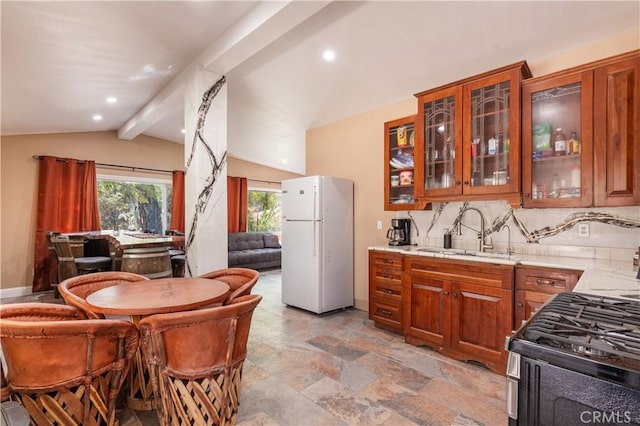 kitchen featuring sink, vaulted ceiling with beams, backsplash, white refrigerator, and gas range