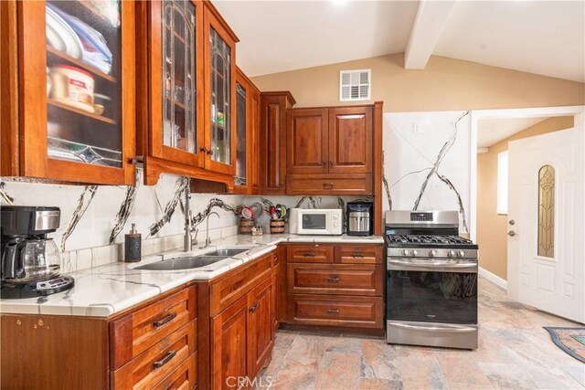 kitchen featuring tasteful backsplash, sink, vaulted ceiling with beams, stainless steel gas range oven, and light stone countertops