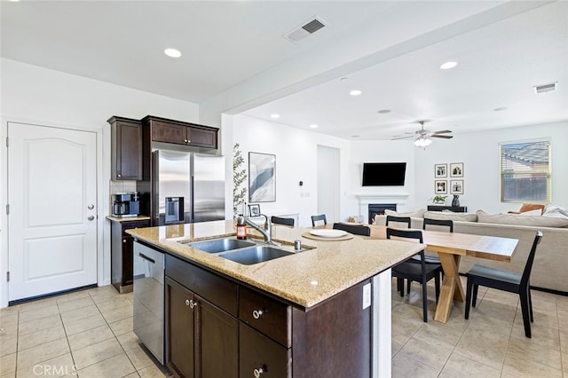 kitchen with light stone countertops, appliances with stainless steel finishes, sink, dark brown cabinetry, and a kitchen island with sink