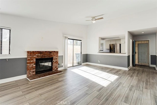 unfurnished living room with light wood-type flooring, a brick fireplace, and ceiling fan