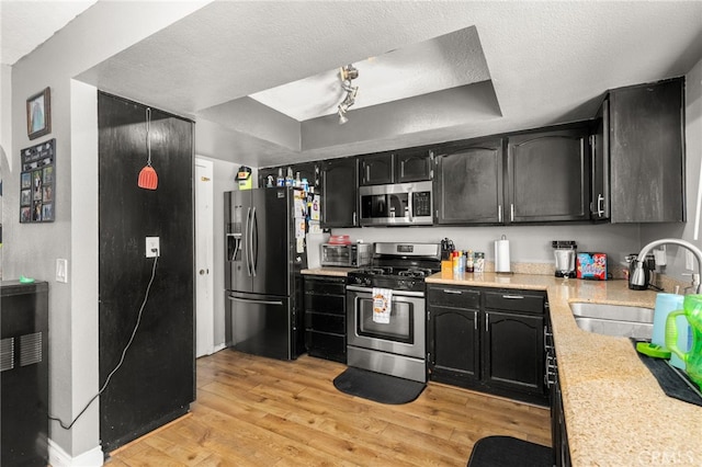 kitchen with a tray ceiling, stainless steel appliances, sink, light wood-type flooring, and a textured ceiling