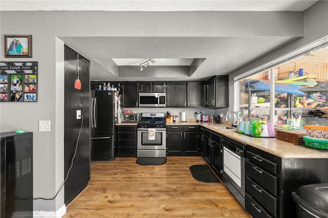 kitchen with stainless steel appliances, a raised ceiling, sink, and light wood-type flooring