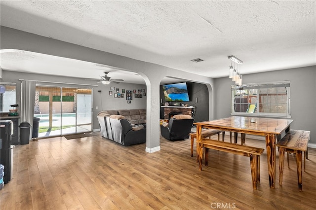 dining room featuring a textured ceiling, wood-type flooring, a fireplace, and ceiling fan