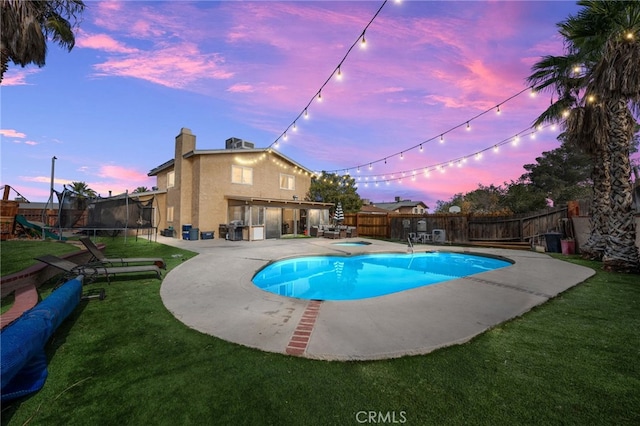 pool at dusk featuring a yard, a trampoline, and a patio area