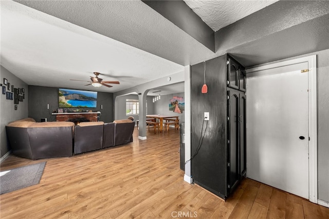 living room with a textured ceiling, light wood-type flooring, and ceiling fan